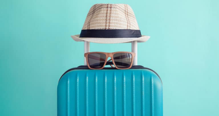 sunglasses and hat on top of a blue suitcase for summer 2021 hotel travel